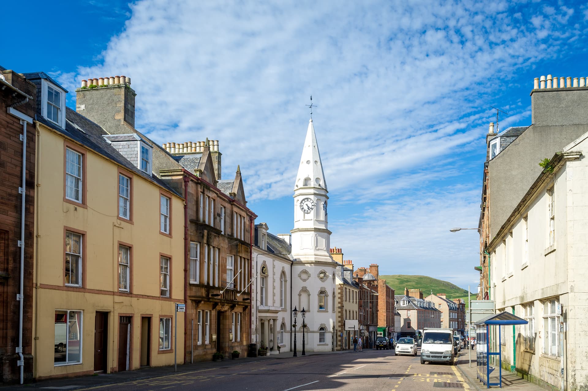 Street scene in Campbeltown featuring historic buildings and a prominent white clock tower under a blue sky.