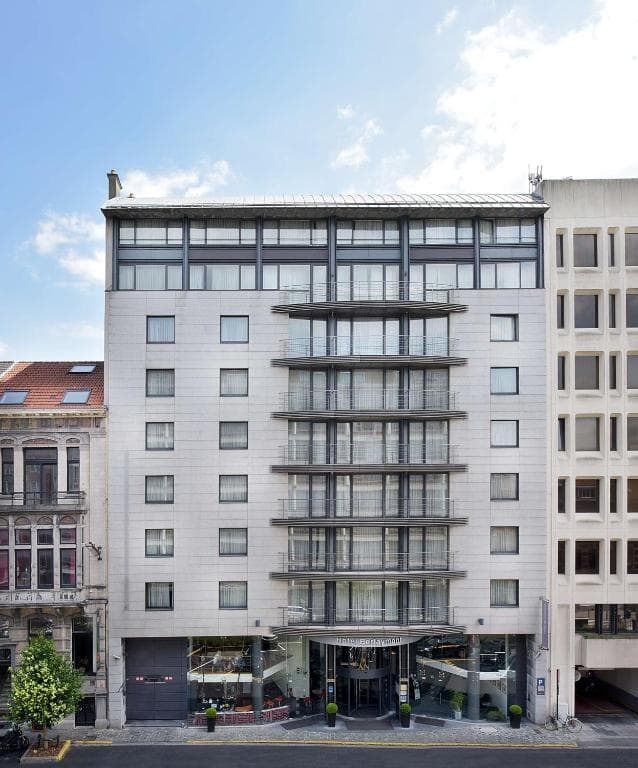 Modern hotel building facade with balconies, flanked by older architecture under a blue sky.