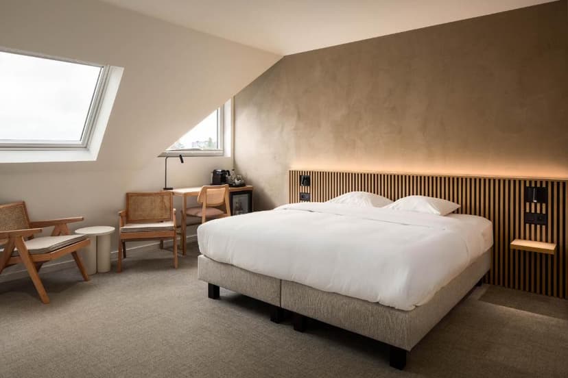 Hotel attic bedroom with white bedding, wooden furniture, and slanted skylight windows.