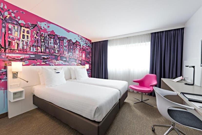 Twin beds in modern hotel room with bright pink cityscape mural and white desk area.