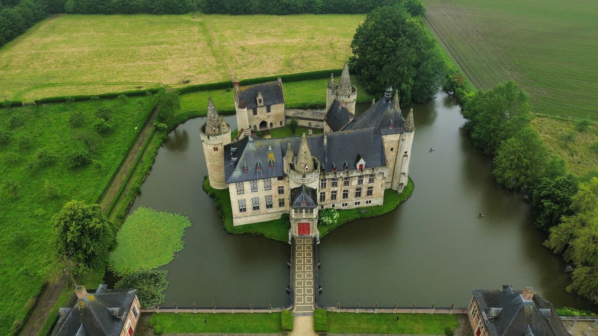 Aerial view of Laarne Castle surrounded by a moat, green fields, and trees.