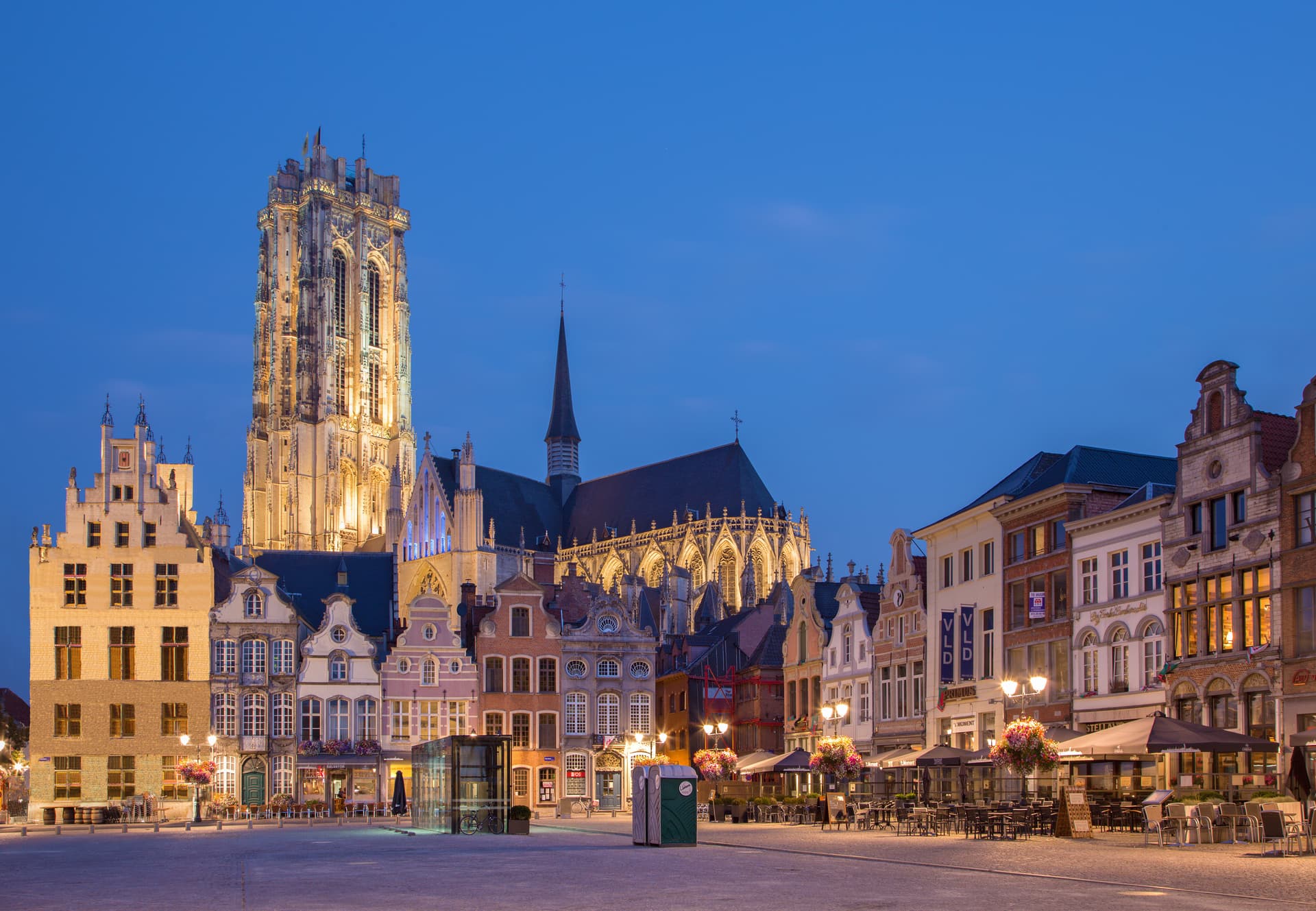 Historic European town square with illuminated cathedral tower and gabled buildings at dusk