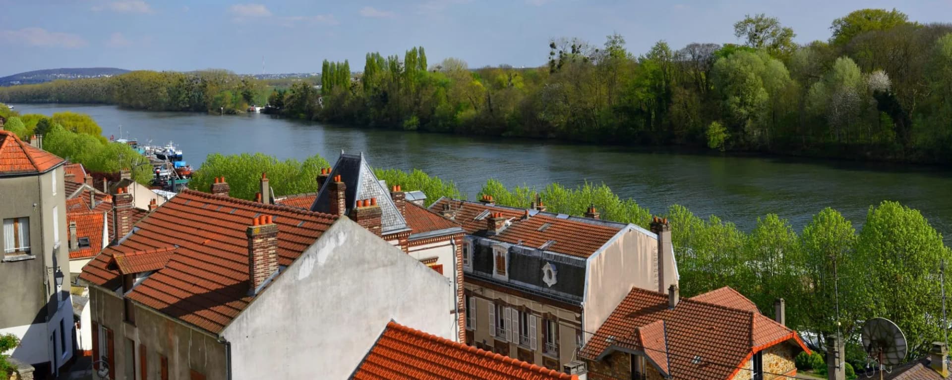 Rooftops of Conflans-Sainte-Honorine overlooking the Seine River with lush green trees.