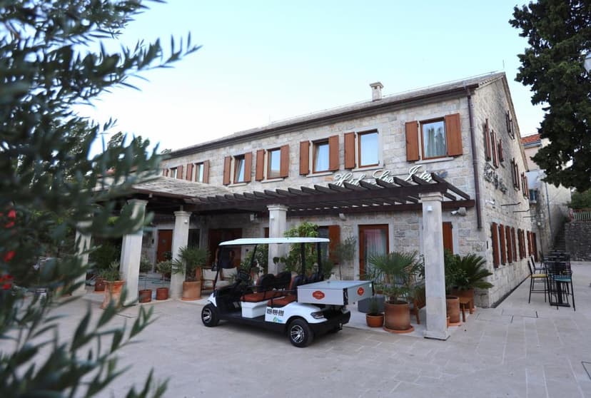 Stone hotel exterior with wooden shutters, golf cart parked, and olive branches in foreground in Trebinje.