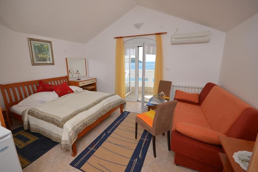 Hotel room with wooden bed, orange sofa, and balcony view of the sea in Herceg Novi.