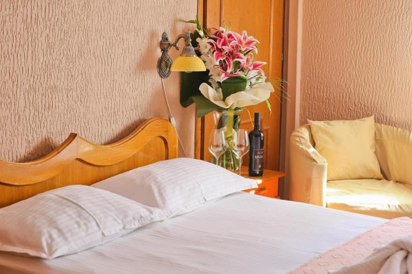 Hotel room with made bed, flowers, wine bottle, and two wine glasses on nightstand.