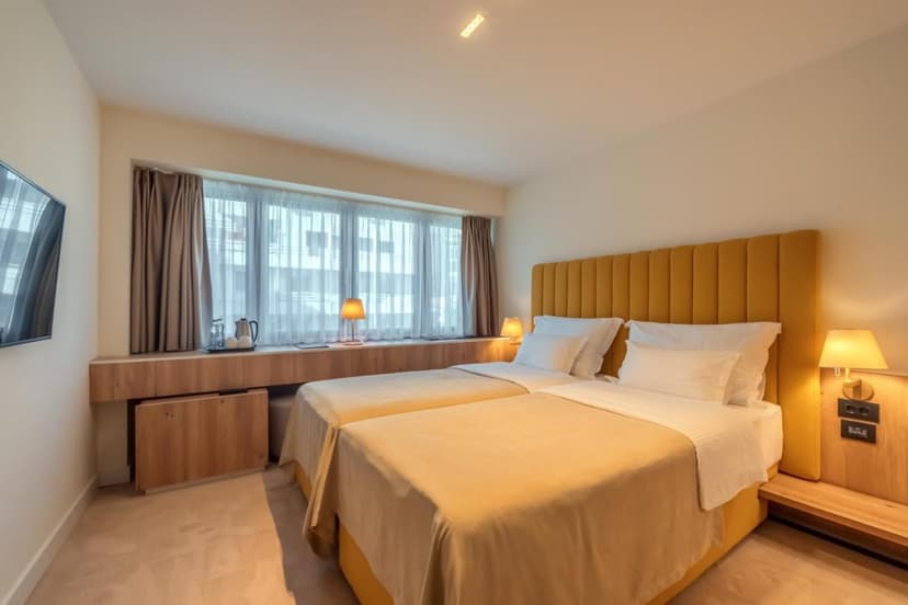 Twin beds with yellow bedding and white pillows in a modern hotel room with city view.