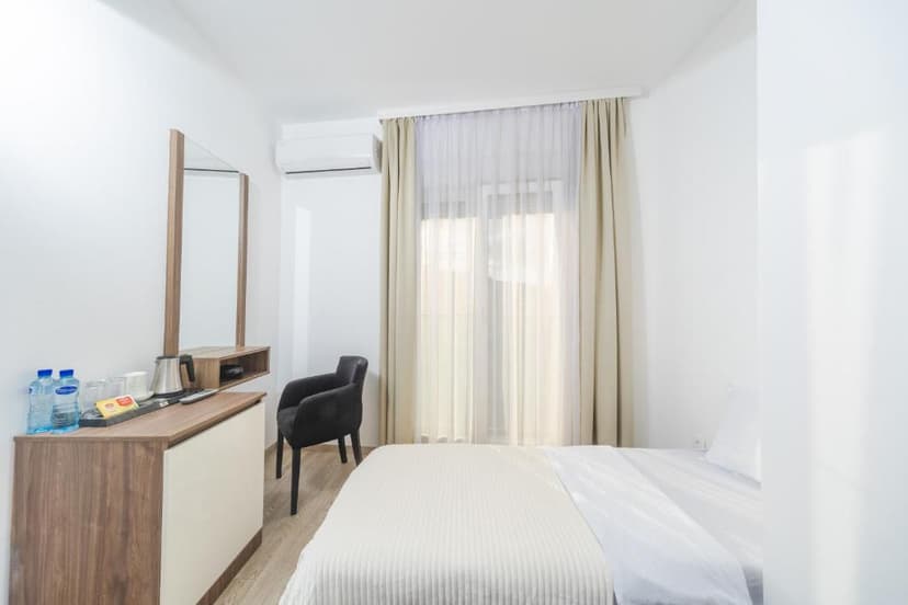 Hotel room with white walls, wood furniture, black chair, and window with beige curtains in Budva