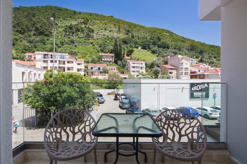 Balcony with two chairs and table overlooking Budva buildings and green hillside.