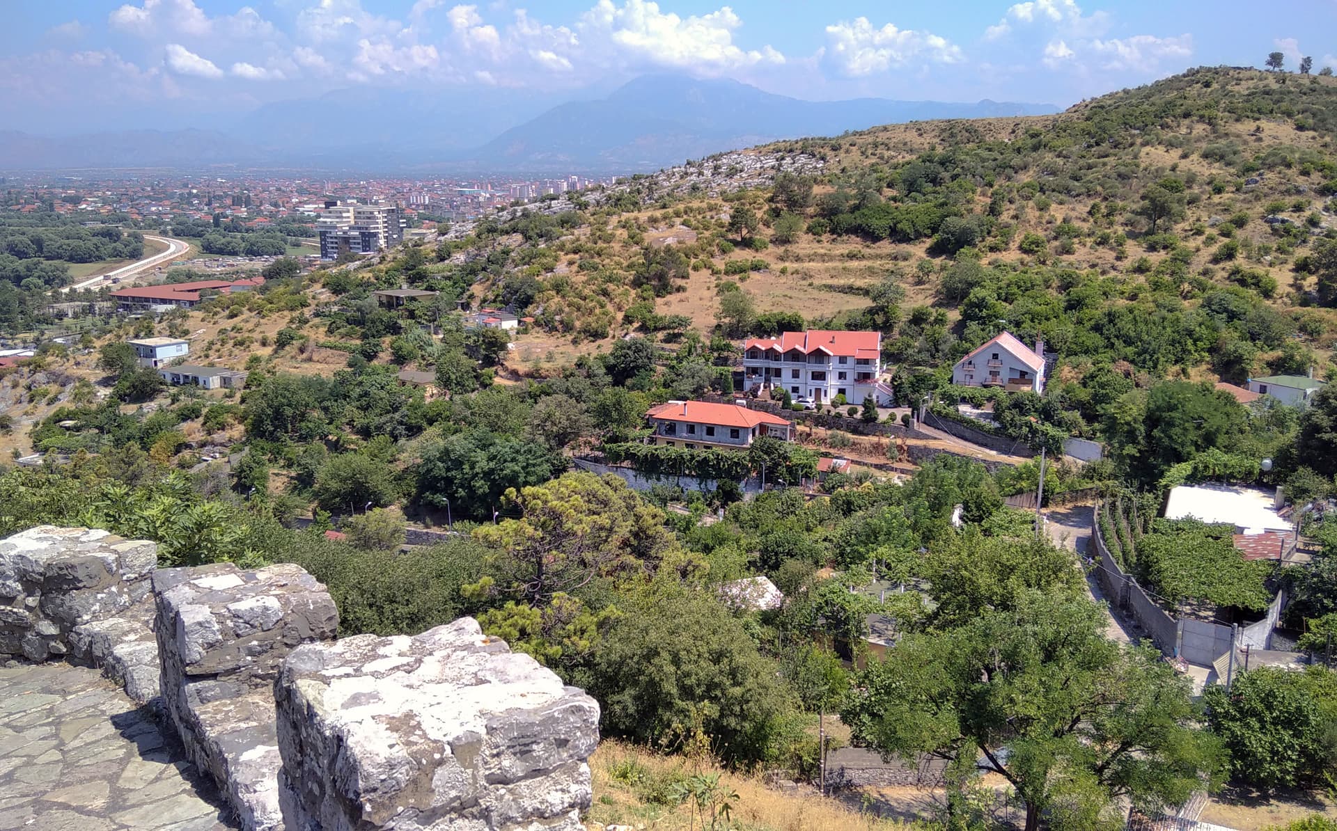 Stone fortress wall overlooking Shkodra, Albania, with city and mountains in background.