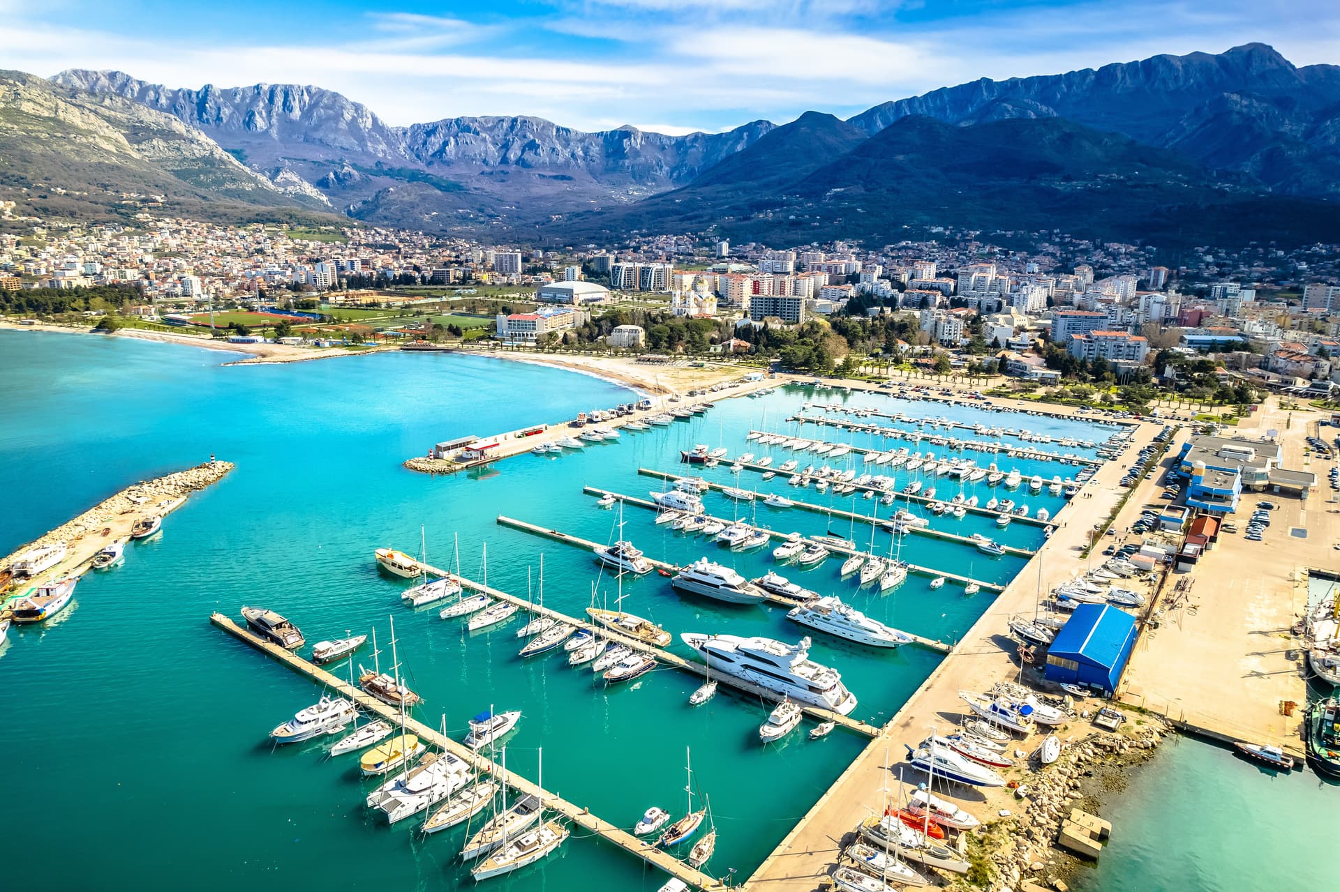 Marina filled with yachts and sailboats against a backdrop of a coastal city and rugged mountains in Montenegro.