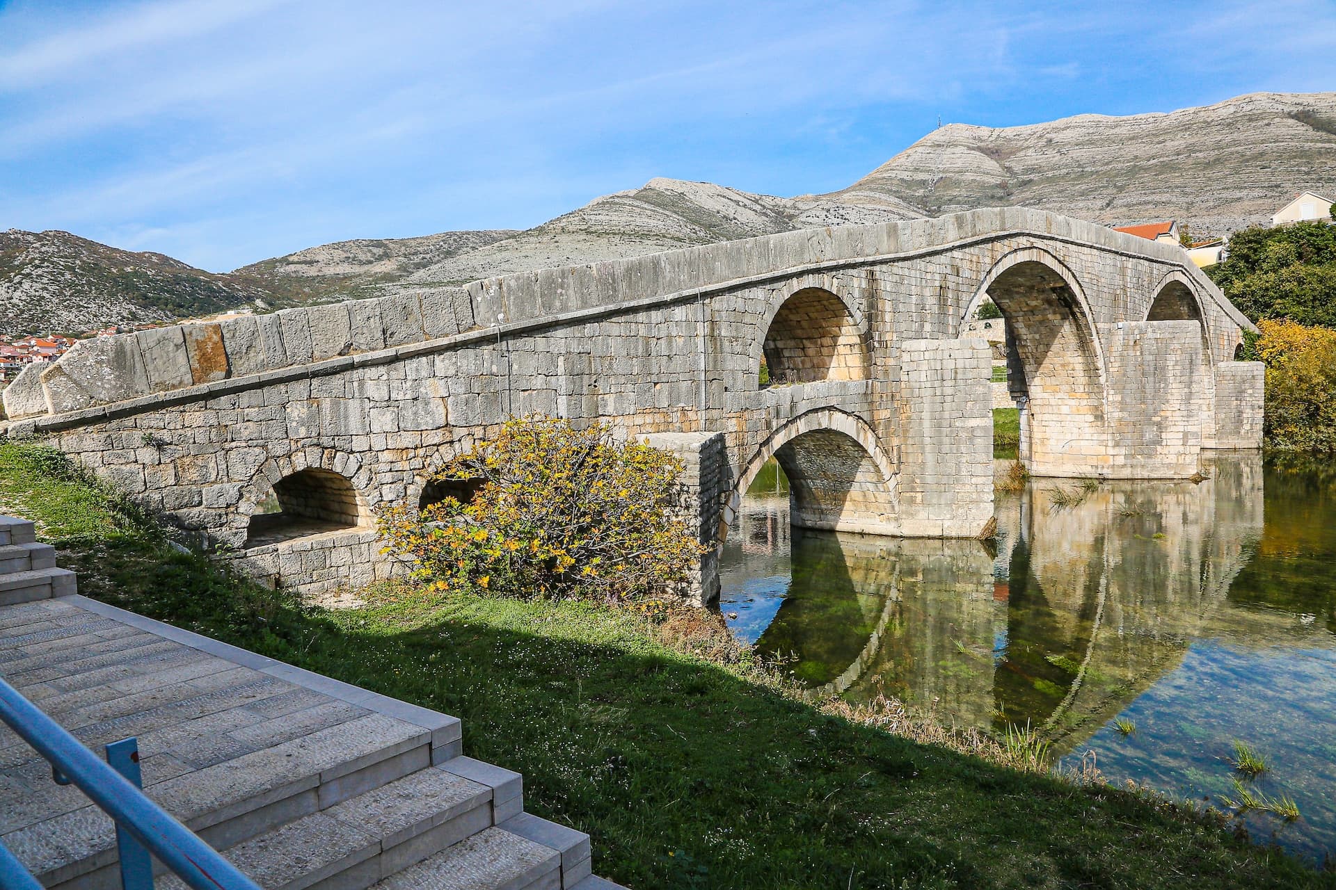 Stone arched bridge over river with reflection, backed by arid mountains in Trebinje, Bosnia and Herzegovina.