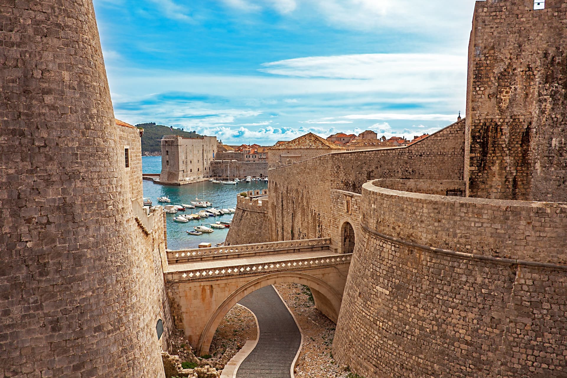 Old Town harbor in Dubrovnik, Croatia, with stone walls, arched bridge, and boats on blue water.