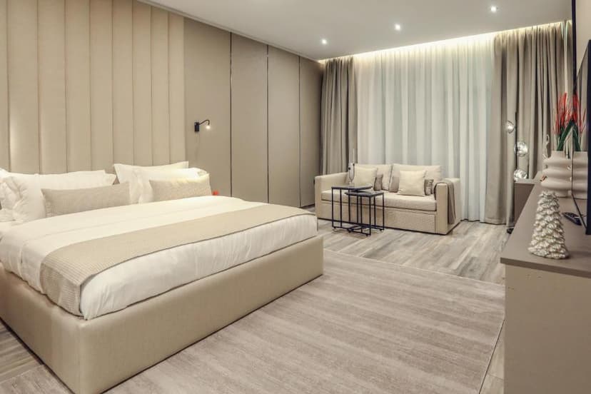 Modern hotel room with beige upholstered bed, sofa, and light wood-look flooring in Hotel Dirista Shkoder.