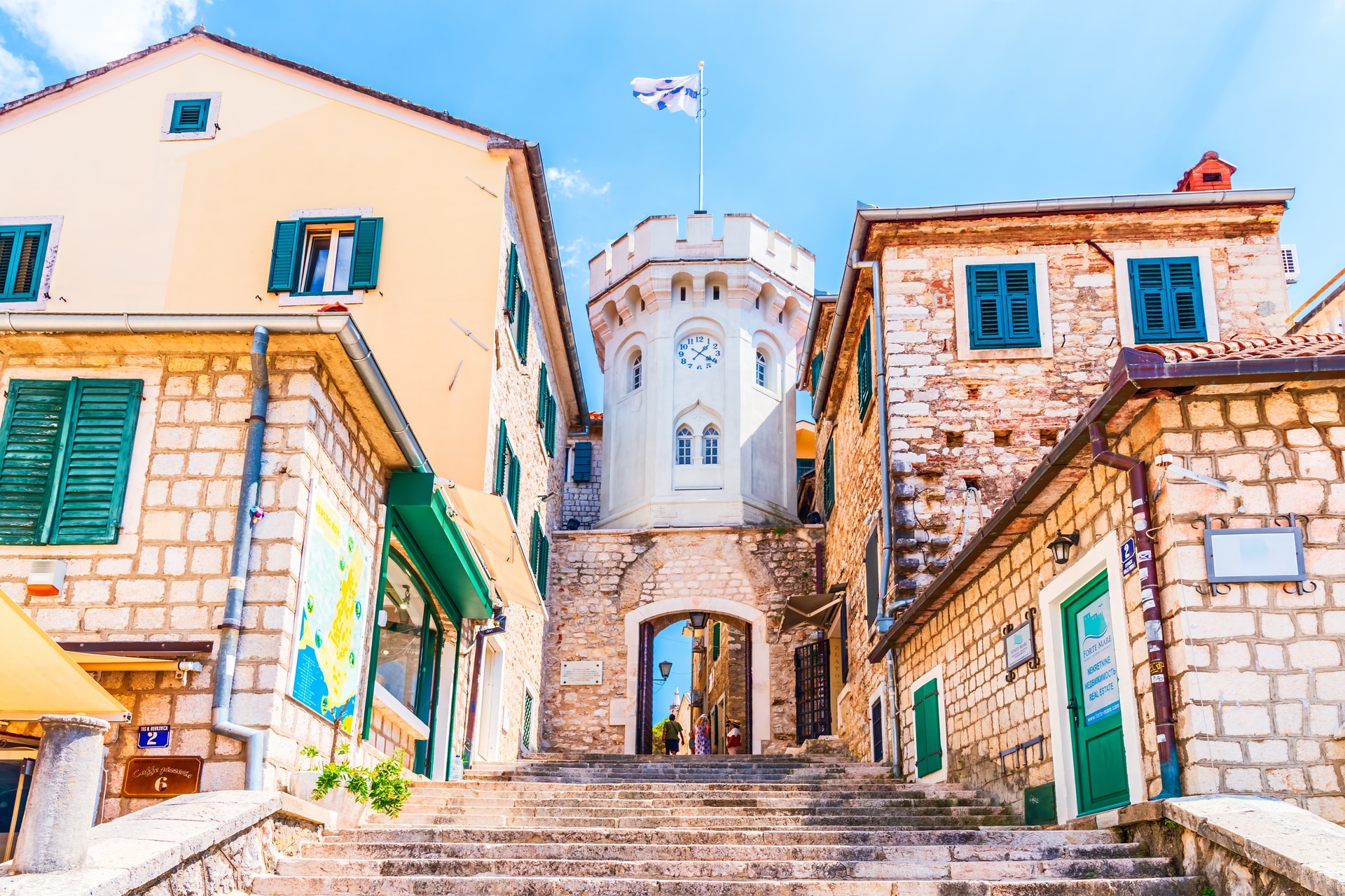 Herceg Novi clock tower gate above stone steps flanked by historic buildings in the old town.
