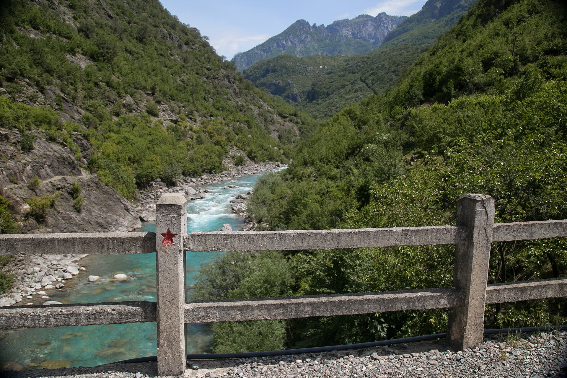 Turquoise river flowing through lush green mountains in Albania, viewed over a concrete railing.