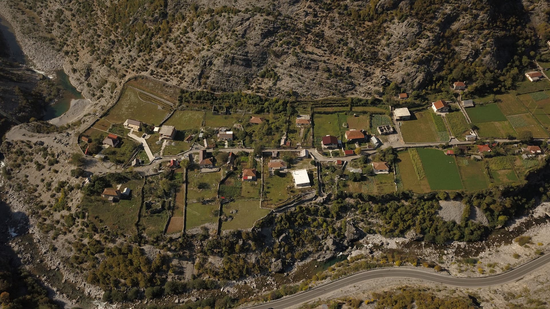 Aerial view of Tamare village in Albania nestled between rocky mountains and a winding river.