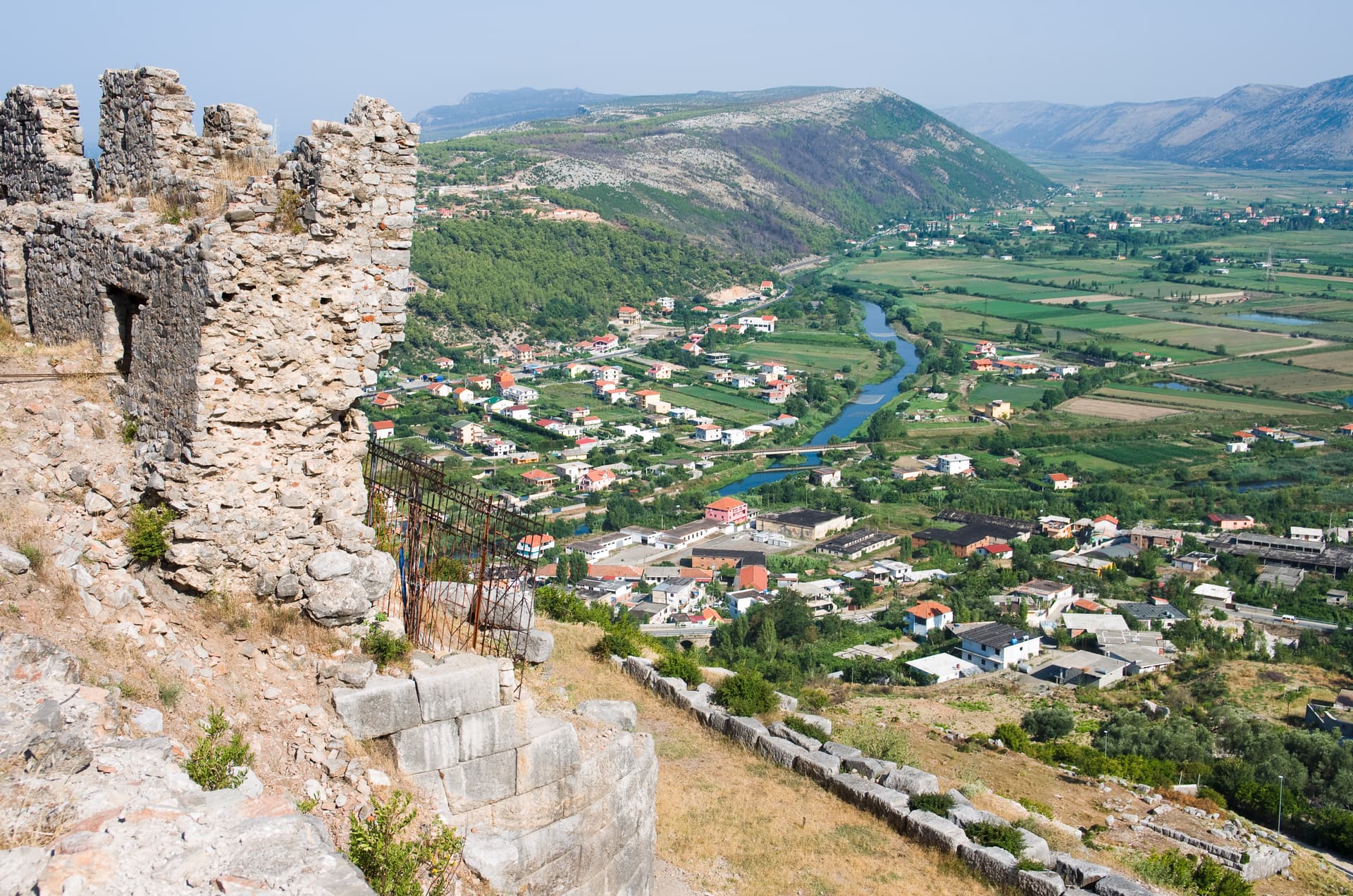 Ruin walls overlooking the town of Lezhe, Albania, with a river and green valley below.