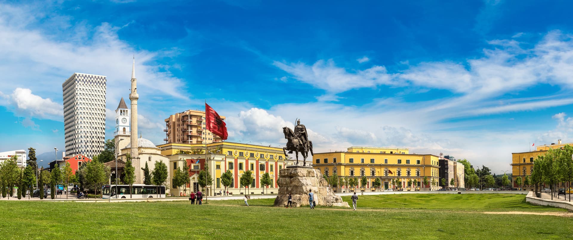 Equestrian statue at Skanderbeg Square, Tirana, with mosque, modern tower, and yellow buildings.