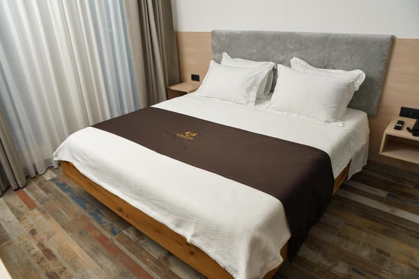 Hotel Albulena Lac room with white bedding, brown runner, and wood-look tile floor.