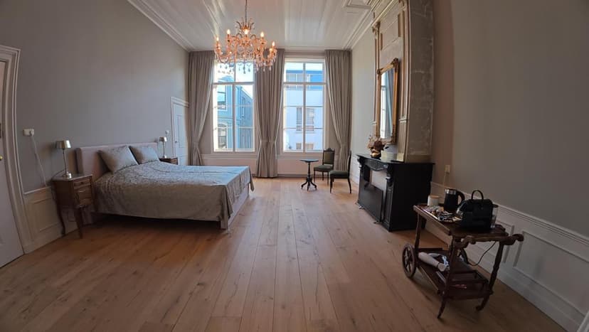 Bedroom with large bed, crystal chandelier, and light wood floor in Dordrecht.