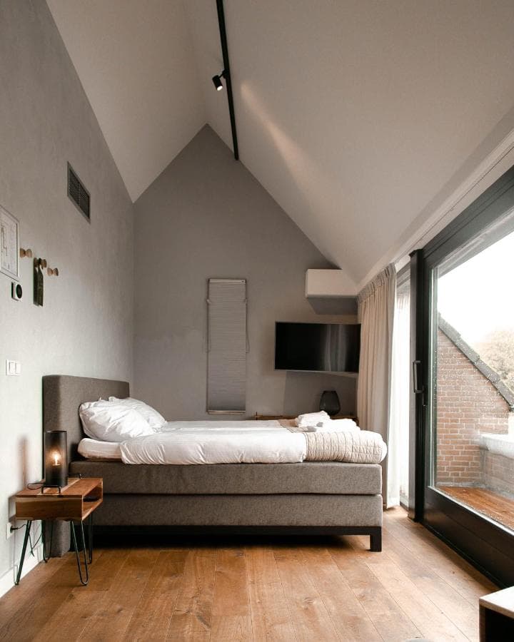 Modern bedroom with sloped ceiling, wood floor, and large glass door to balcony.