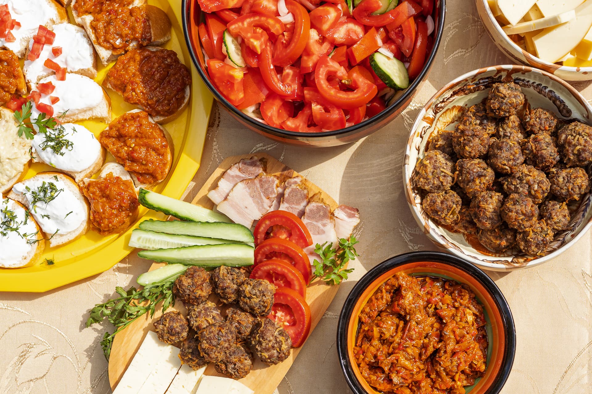 Platter of Transylvanian cuisine including meatballs, cheese, cured meat, bread with spreads, and tomato salad.