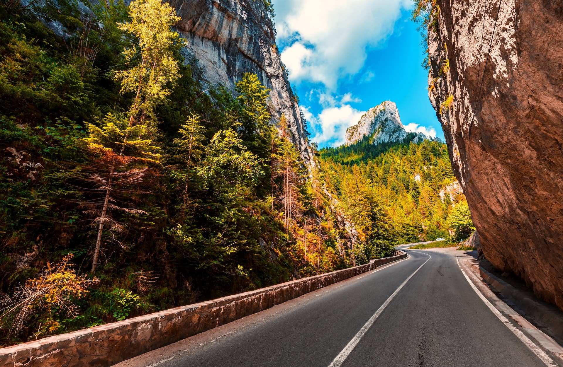 Winding mountain road through a gorge with steep cliffs and autumn forest in the Carpathian Mountains.