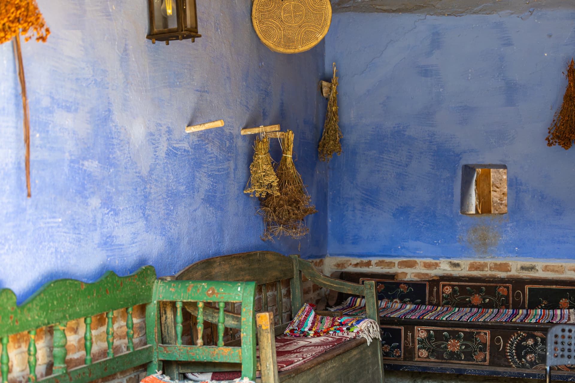 Rustic interior with bright blue walls, painted wooden benches, and dried herbs hanging from the wall.
