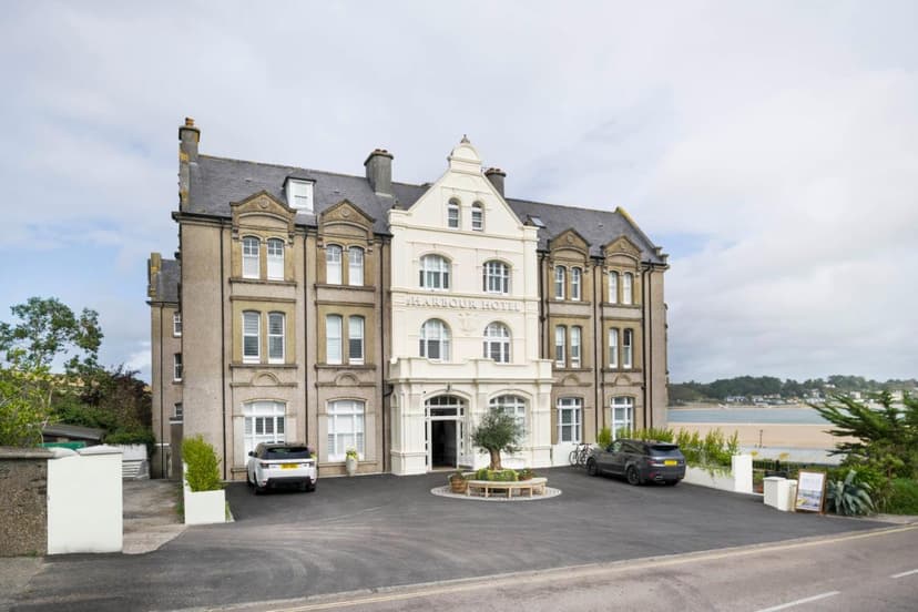 Harbour Hotel building with parked cars and view of sandy beach and coastal town.