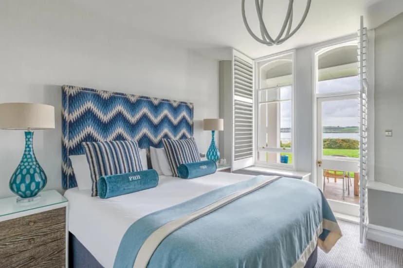 Bedroom with blue patterned headboard overlooking water and green lawn in Padstow