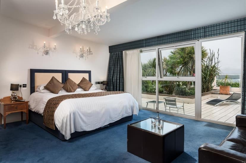 Hotel bedroom with crystal chandelier, blue carpet, and patio access with lounge chairs