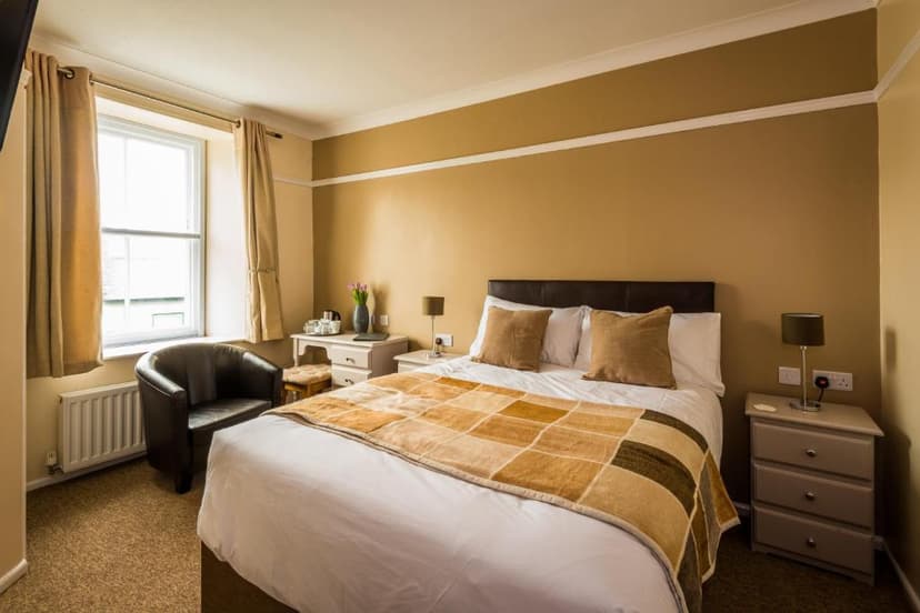 Cozy hotel bedroom with double bed, brown armchair, window, and tan walls