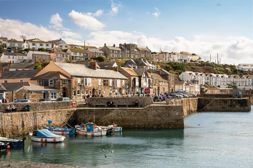 Fishing boats moored in a harbor with stone quays and colorful houses climbing a hillside.