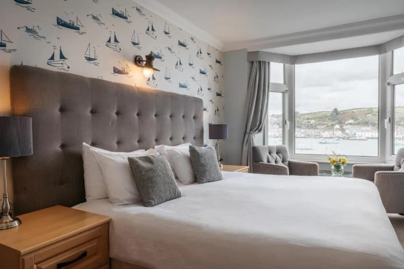 Bedroom with boat wallpaper, large window view of harbor town, and white bedding.