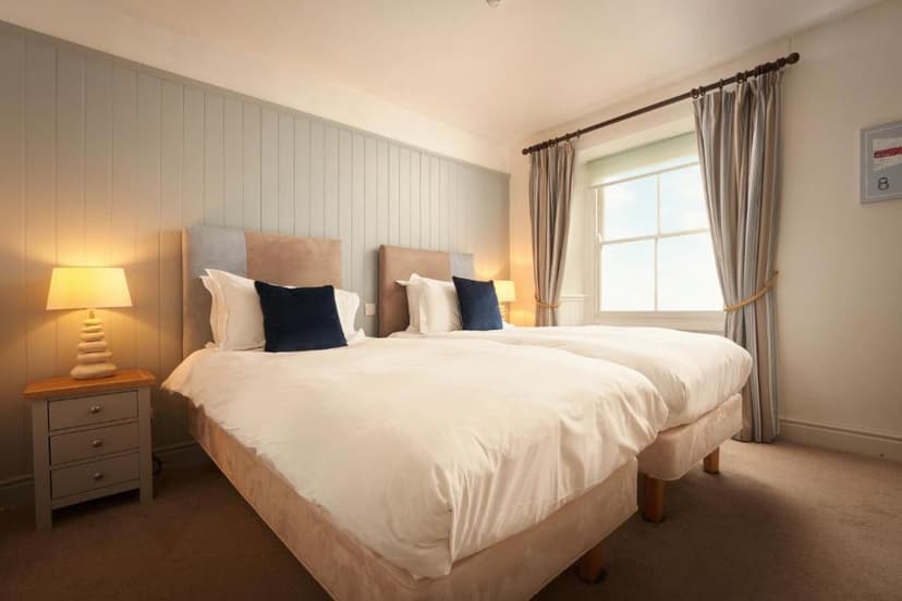 Twin beds with white duvets and navy pillows in a room with paneled walls and bright window.
