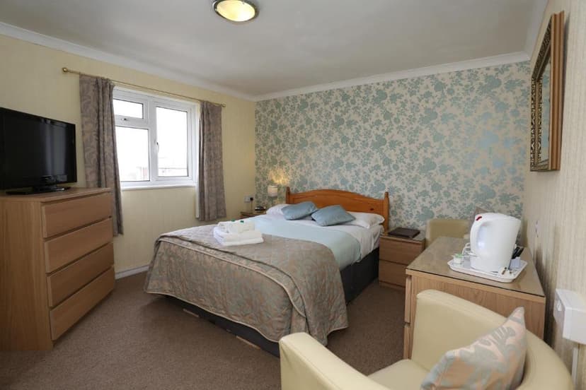Bedroom with double bed, floral wallpaper, television, and hospitality tray with kettle.
