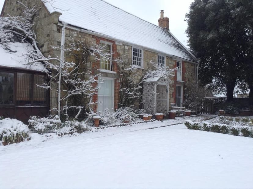 Stone cottage with snow-covered roof and yard, bare tree branches dusted with snow.