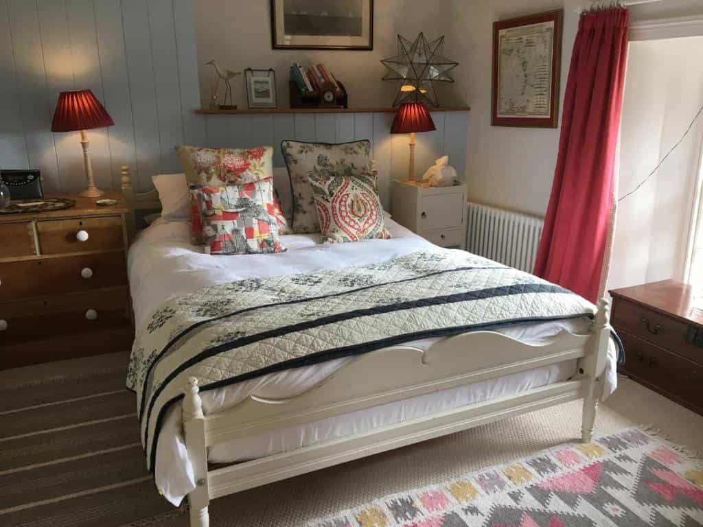 Cozy bedroom with white bed, patterned quilt, red lampshades, and colorful rug