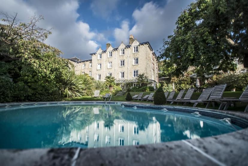 Outdoor swimming pool reflecting a stone hotel building surrounded by lush green trees.