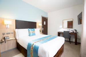 Hotel bedroom with double bed, light blue accent wall, and wooden desk area.
