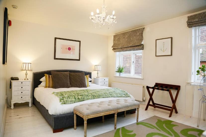 Bedroom with dark upholstered bed, chandelier, white wood floors, and framed anchor art.