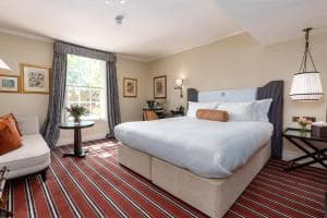 Hotel bedroom with large white bed, patterned red rug, and window with dark curtains.