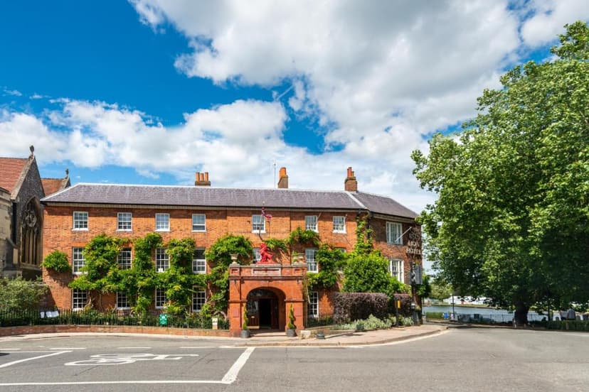 Brick hotel building covered in ivy with a red lion statue above the entrance under a blue sky.
