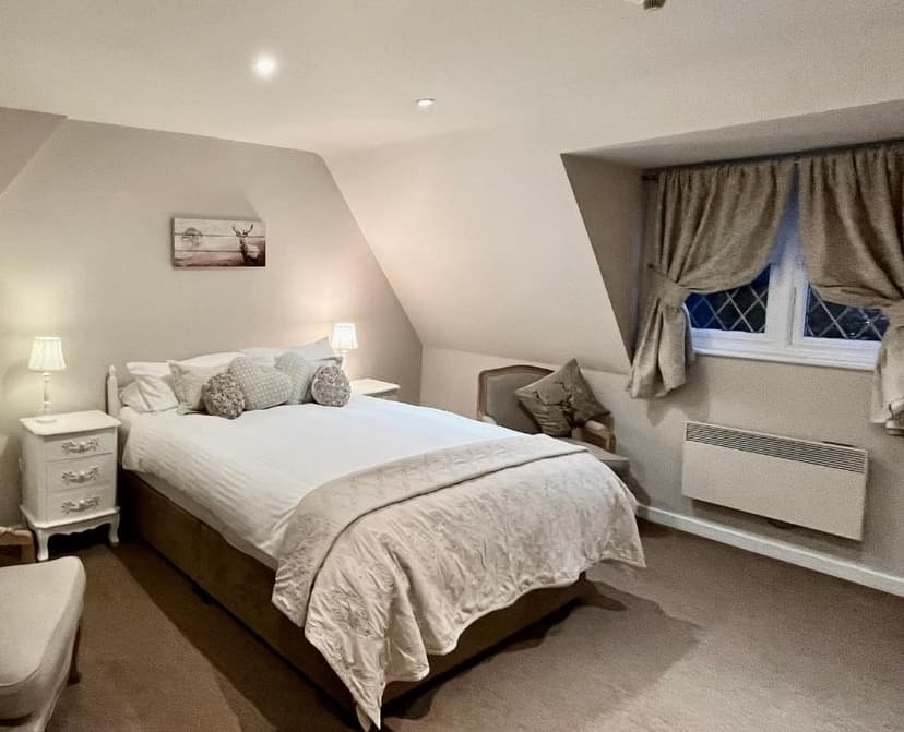 Cozy attic bedroom with double bed, bedside lamps, and window with tie-back curtains