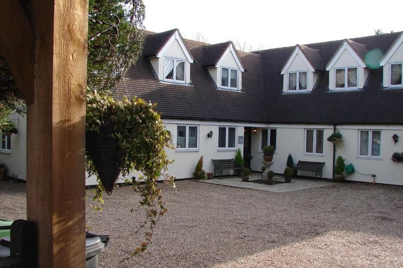 White building with dormer windows and gravel courtyard, foreground wooden post with hanging plant.