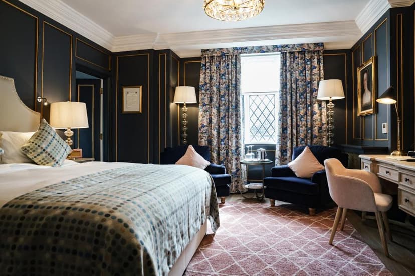 Luxurious hotel bedroom with dark paneled walls, patterned curtains, and a large bed.