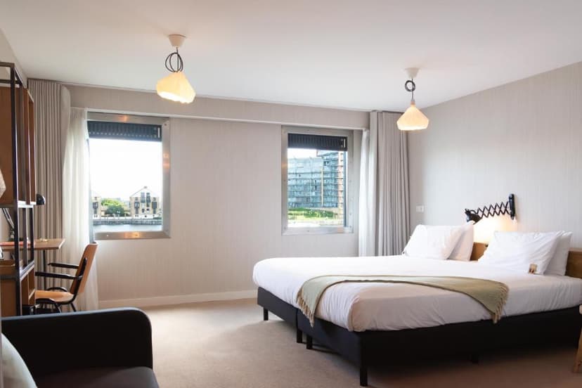 Modern hotel room with white bedding, view of water and buildings through windows