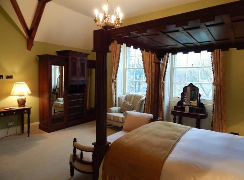 Bedroom with dark wood four-poster bed, antique wardrobe, and large windows.