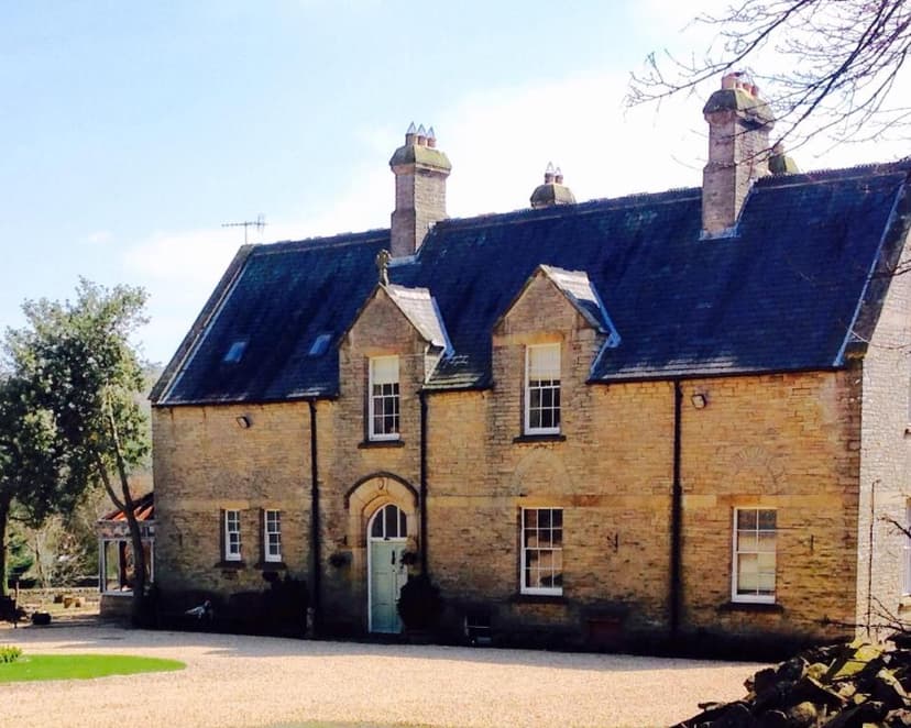 Stone country house with dark slate roof and gravel driveway under clear sky